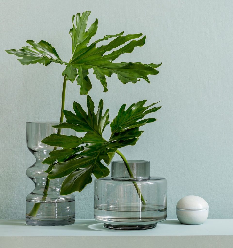 Minimalistic interior design of living room at nice apartment with stylish shelf, glassy vases with tropical flowers and elegant accessories. Copy space. Eucalyptus color concept. Template.